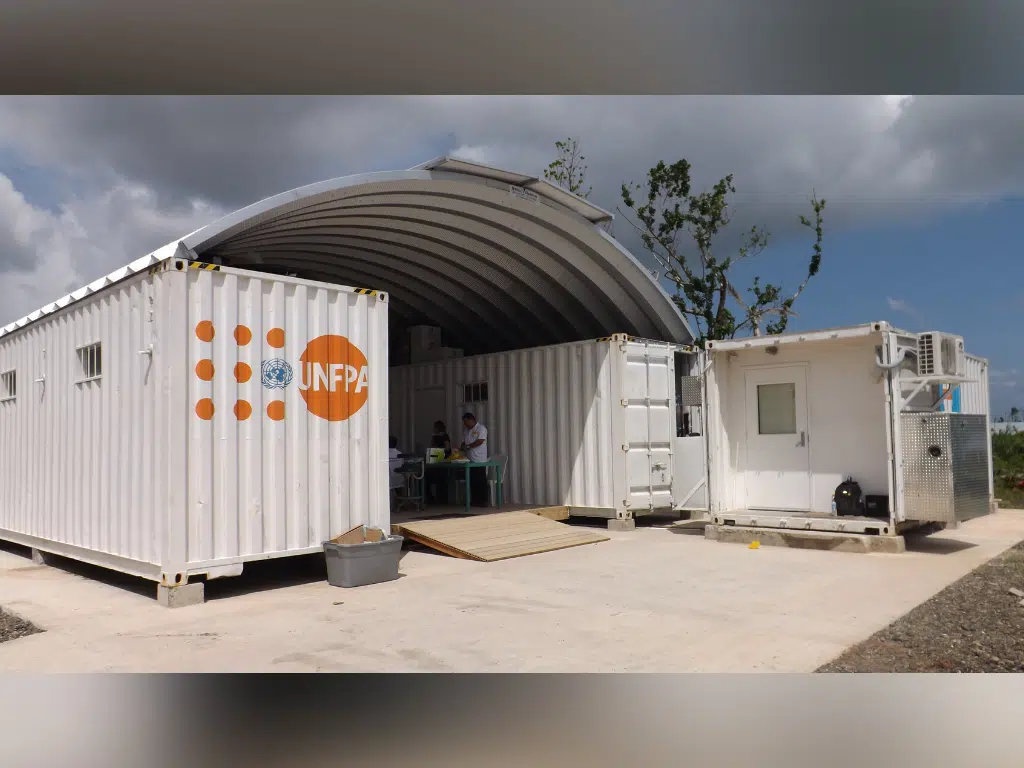 "Clinic in a can" medical relief shelter fashioned out of a arch roof system set on white freight containers.