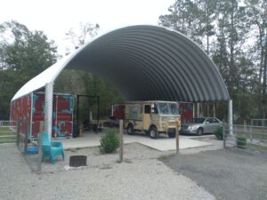 steel arch roof mounted on multicolor red and blue shipping containers with vehicles stored underneath