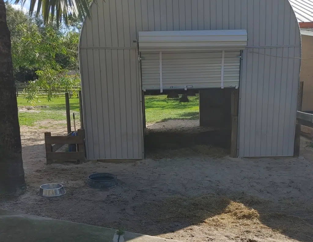 partially opened rolling doors on Quonset structure on top of dirt, water bowls outside