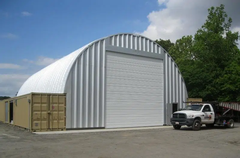Metal container cover workshop set on top of freight containers, steel endwall, large garage door with white truck out front.