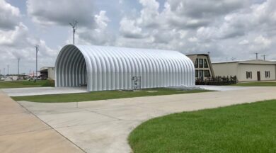 side view of open ended metal quonset hut hangar at small airport with planes in the distance