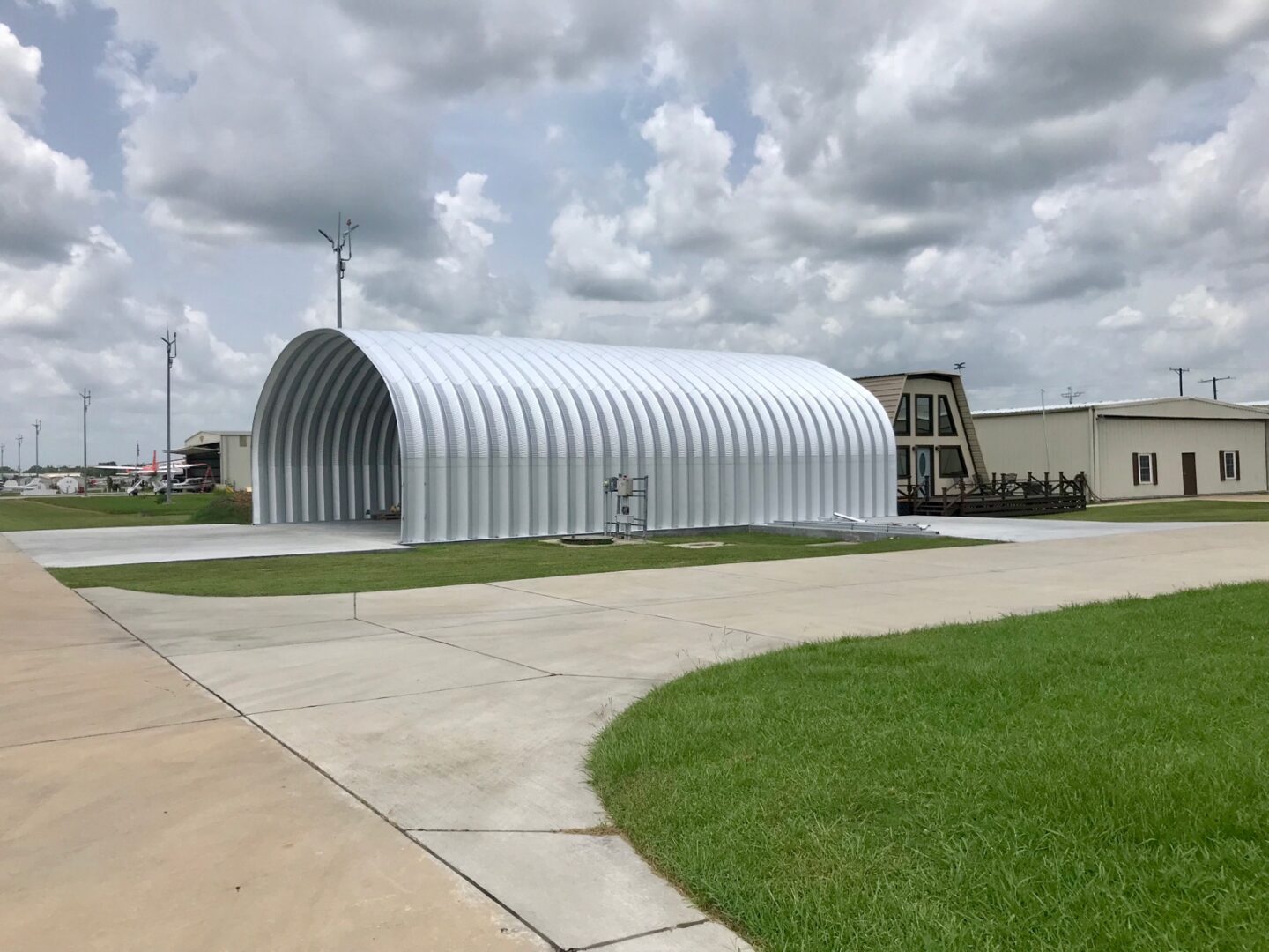 side view of open ended metal quonset hut hangar at small airport with planes in the distance