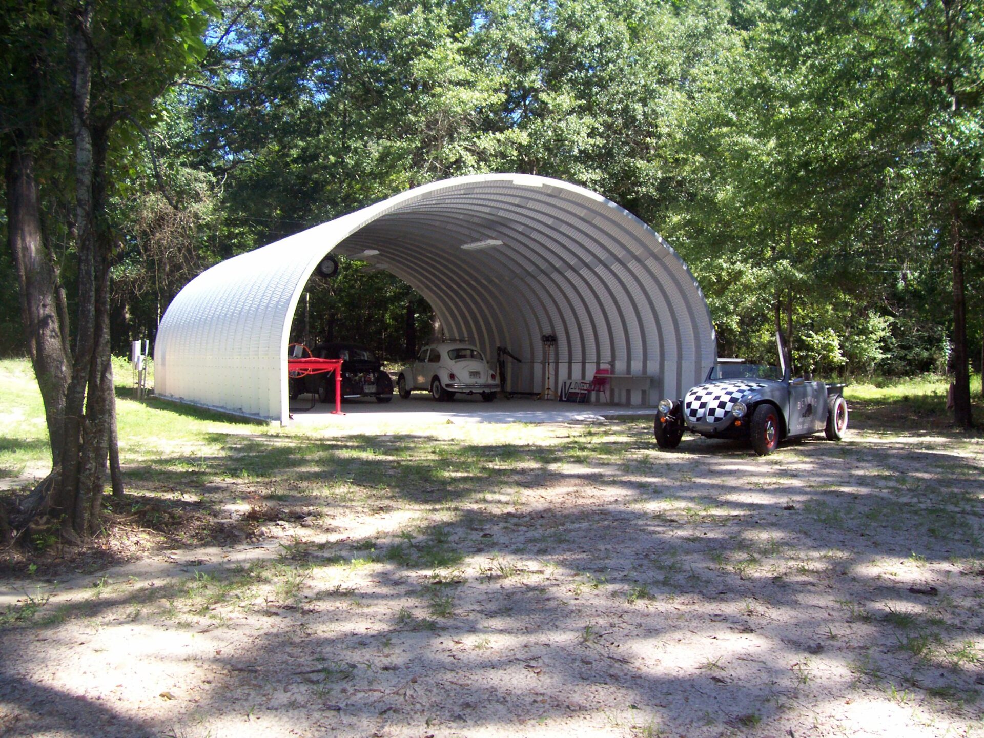 S-Model Quonset hut with no end walls, a checkered race car in front, a white Buggy inside, another car inside, and a red bench inside.