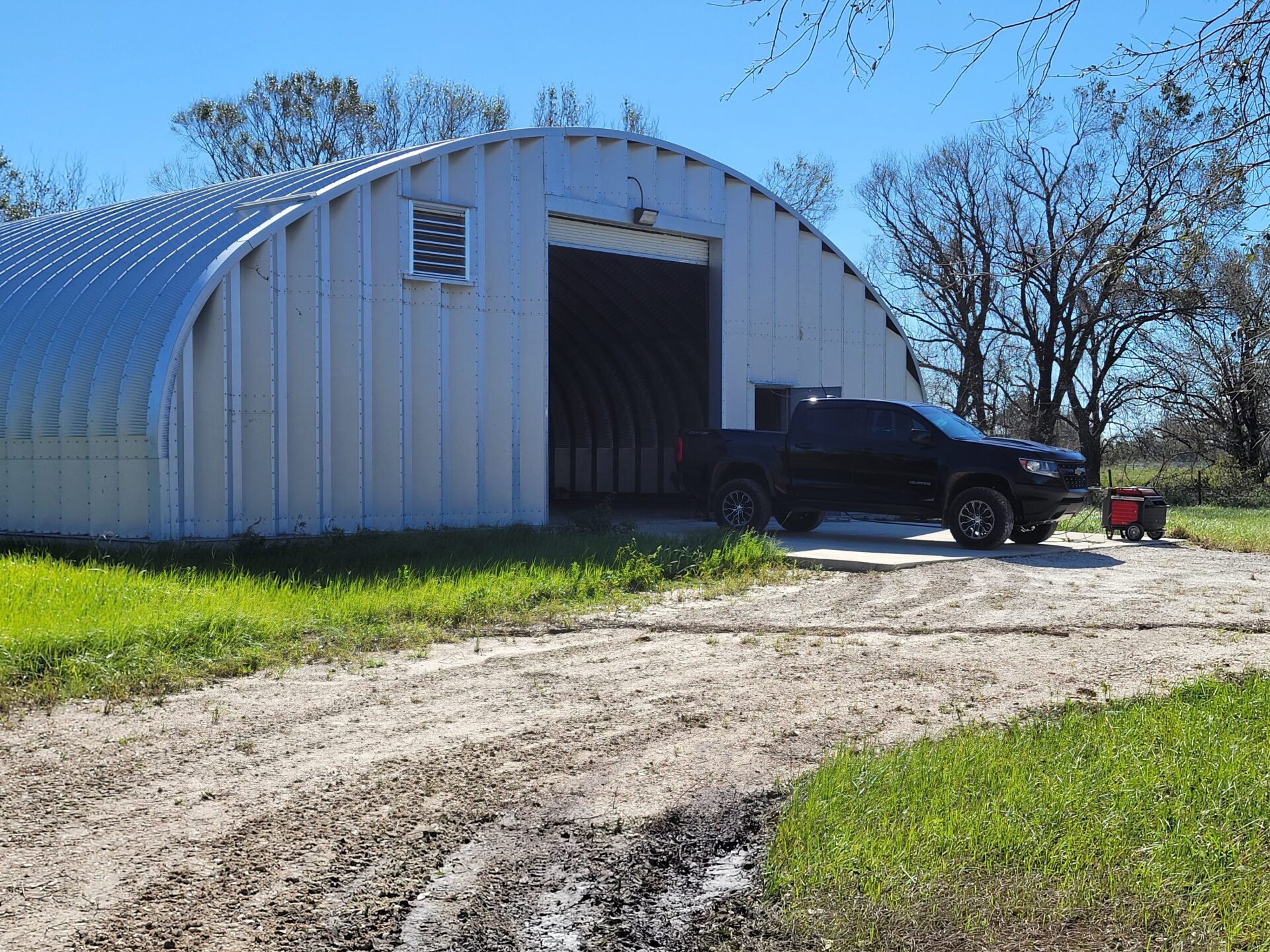 S-Model Quonset hut with steel end wall, vent up top, a black truck in front, and a mud trail leading to the building.