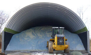 arch steel roof mounted on concrete walls and solid back endwall with pile of salt inside with tractor in front