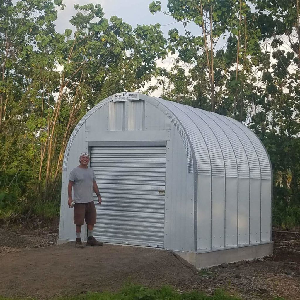 Tiny S-Model Quonset hut with steel endwall, metal rolling door, and man standing out front.