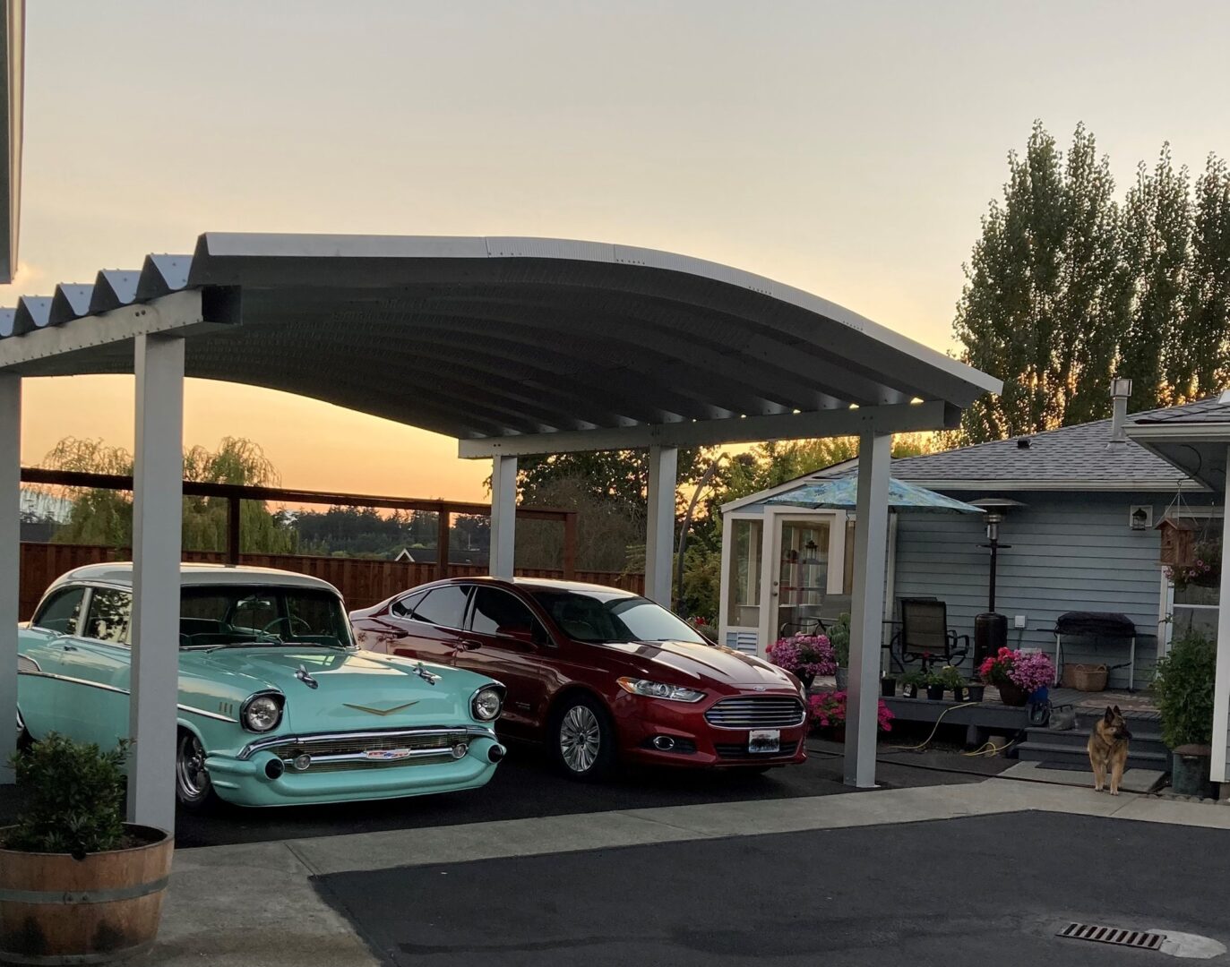 A teal vintage vehicle parked next to a red vehicle underneath a steel carport