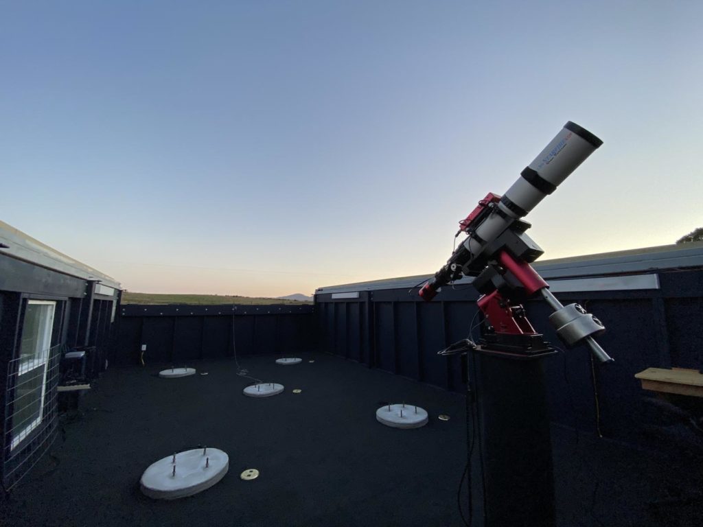Open roof observatory, telescope pointing towards darkening sky.
