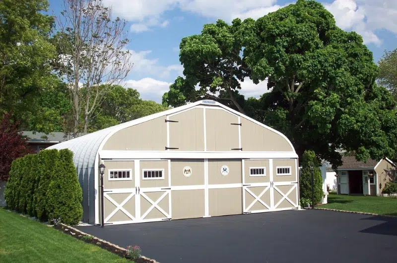 Residential A-model Quonset structure with a custom tan and white endwall, two sets of doors, and large driveway.
