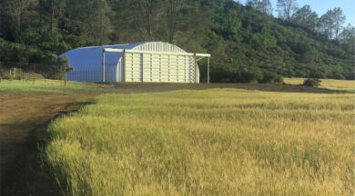 field with metal quonset hut in the distance with a silver front endwall and sliding hangar doors
