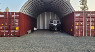 steel arch roof mounted on two red shipping containers with solid rear steel endwall and a boat inside of the structure