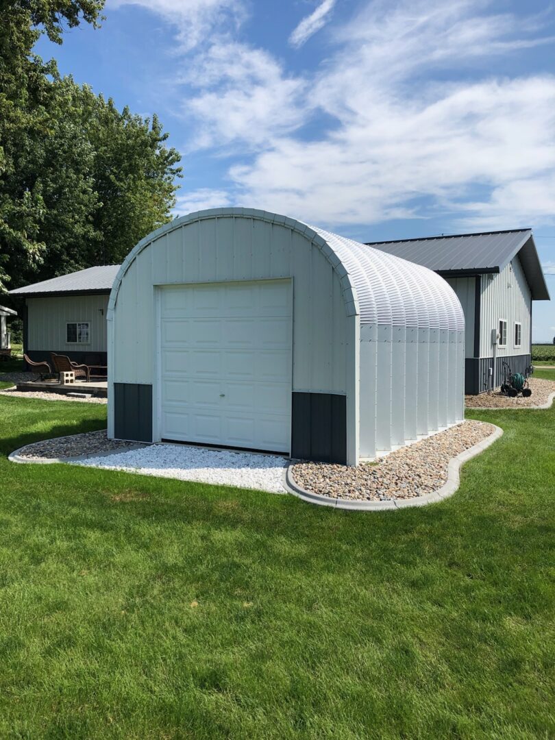 steel S model storage shed with custom white and grey front endwall and landscaping around the building and house behind it