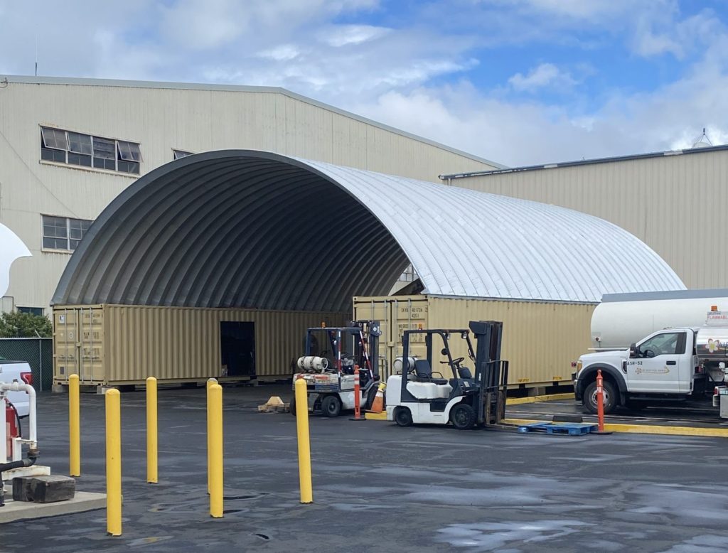 Container cover building, trucks and machinery outside.