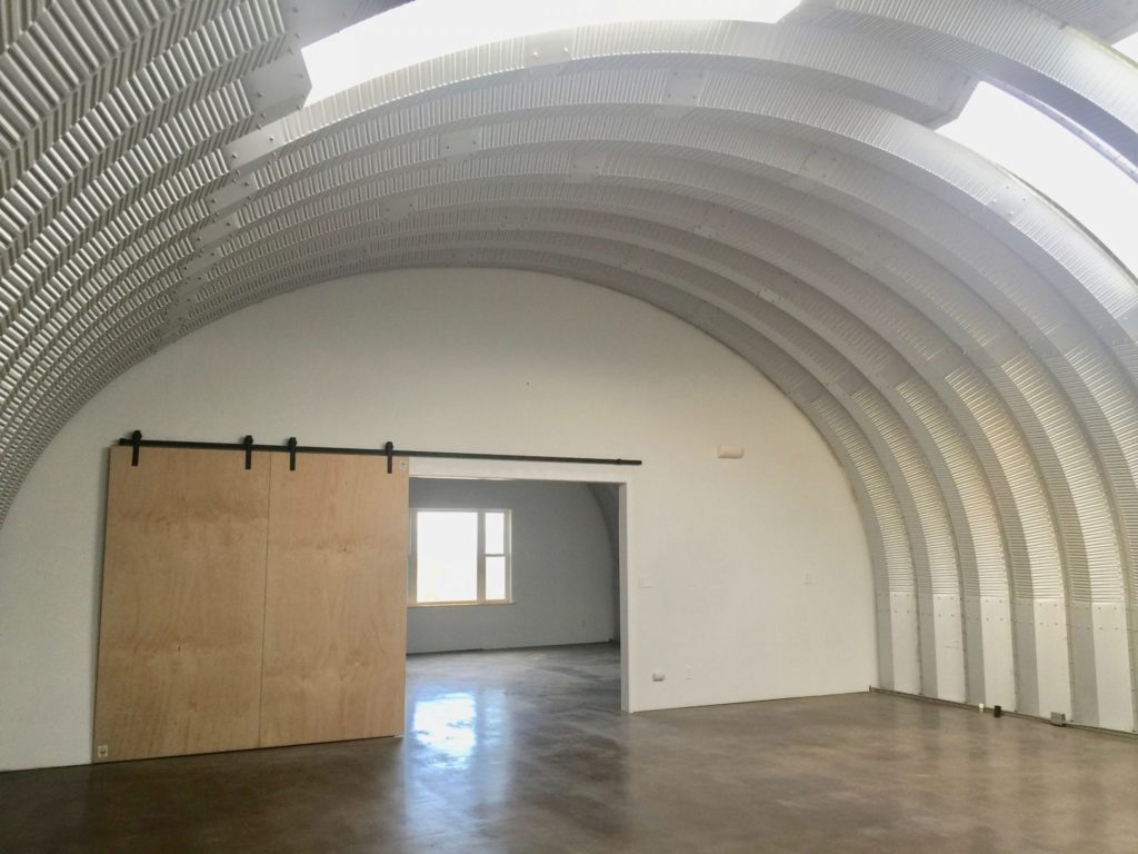 Inside a Quonset hut: skylights, front windows, and sliding barn doors.