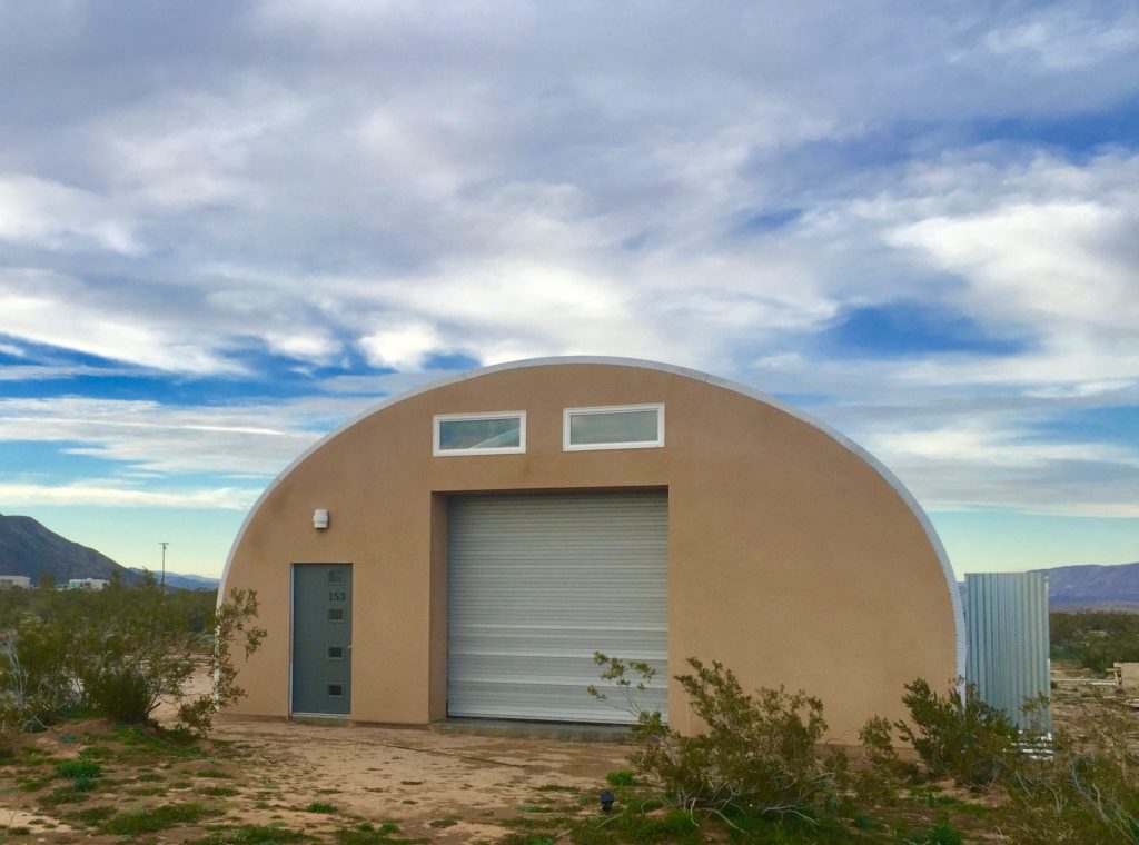 S-model Quonset with custom tan endwall, green door, upper windows, and recessed rolling door.