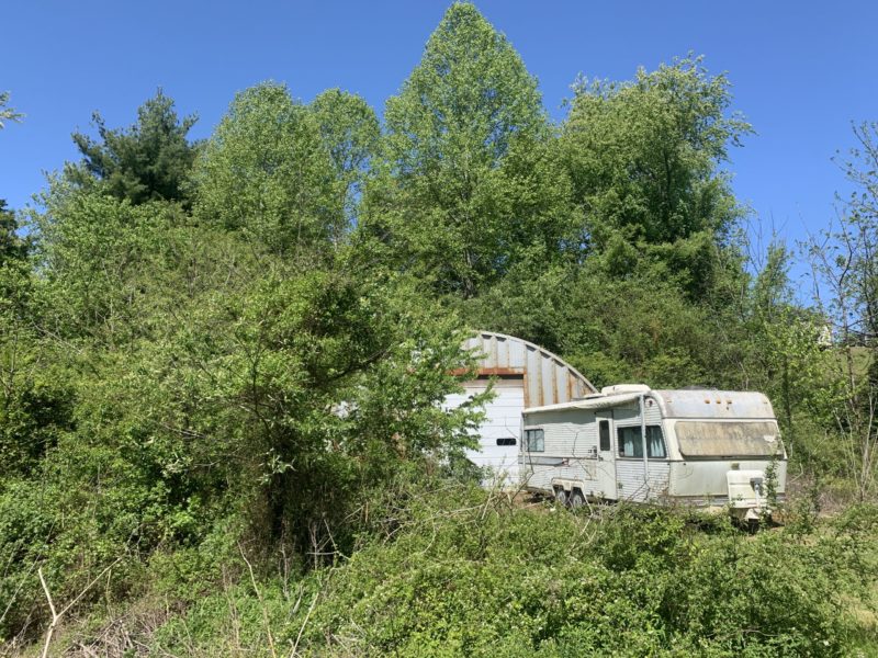 Aged quonset workshop hidden by RV, trees and brush.