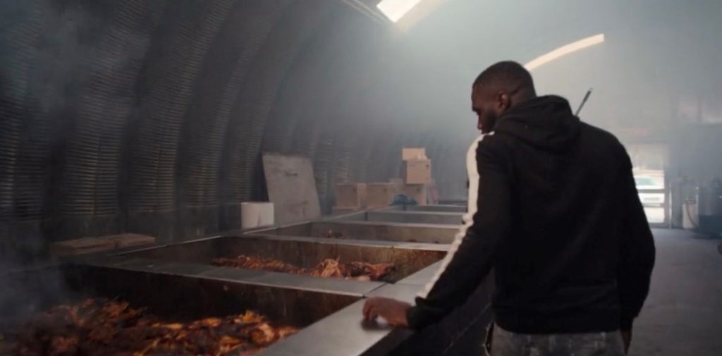 Worker checking on BBQ inside of metal Quonset structure with skylights.