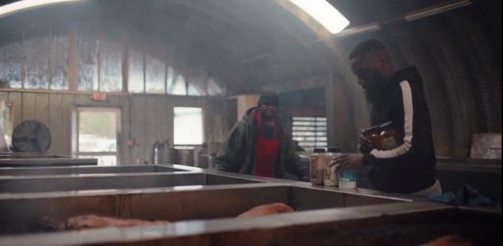 Two workers inside a Quonset hut BBQ pit seasoning meat.