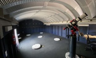 Inside small observatory, steel arched roof, telescope.