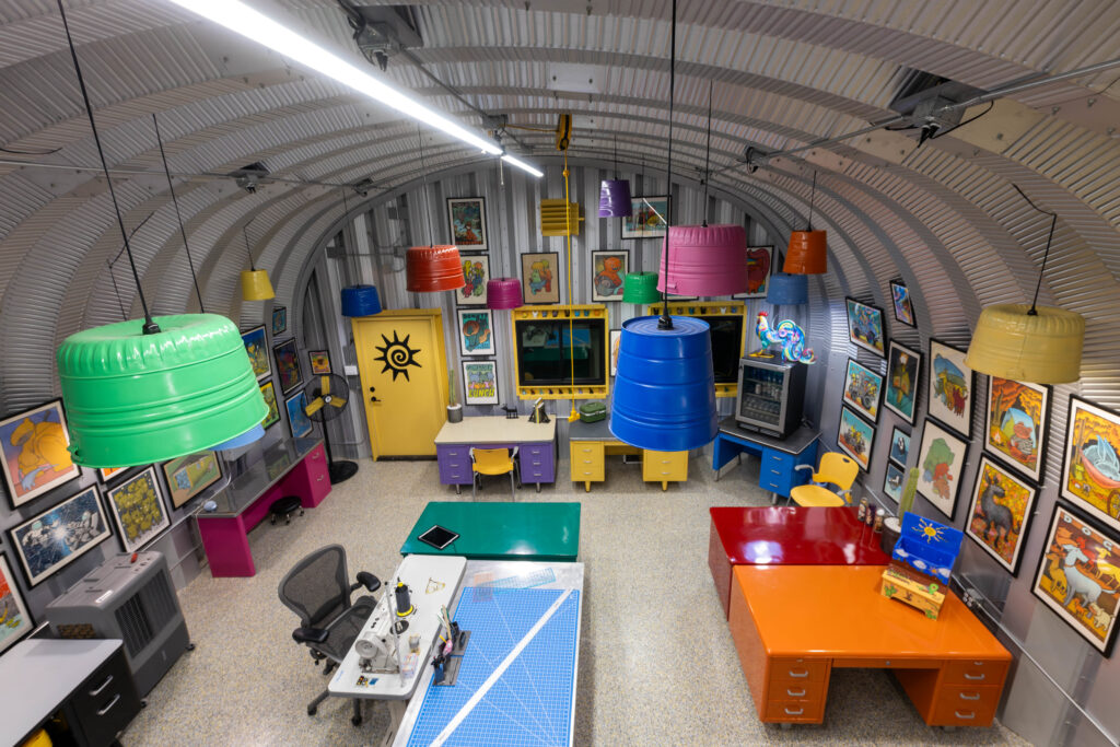 Inside of an S-Model Quonset hut with multi-colored lights, multi-colored desks, and painting all around the room.