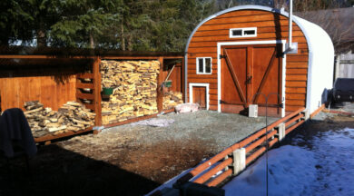 steel S model storage shed with custom wood front endwall and wood stove inside and stacks of fire wood