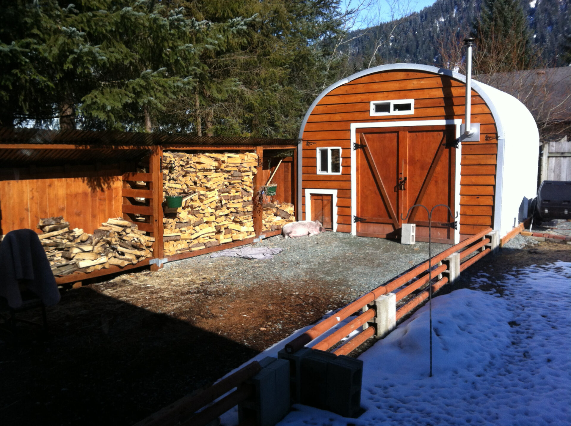 steel S model storage shed with custom wood front endwall and wood stove inside and stacks of fire wood