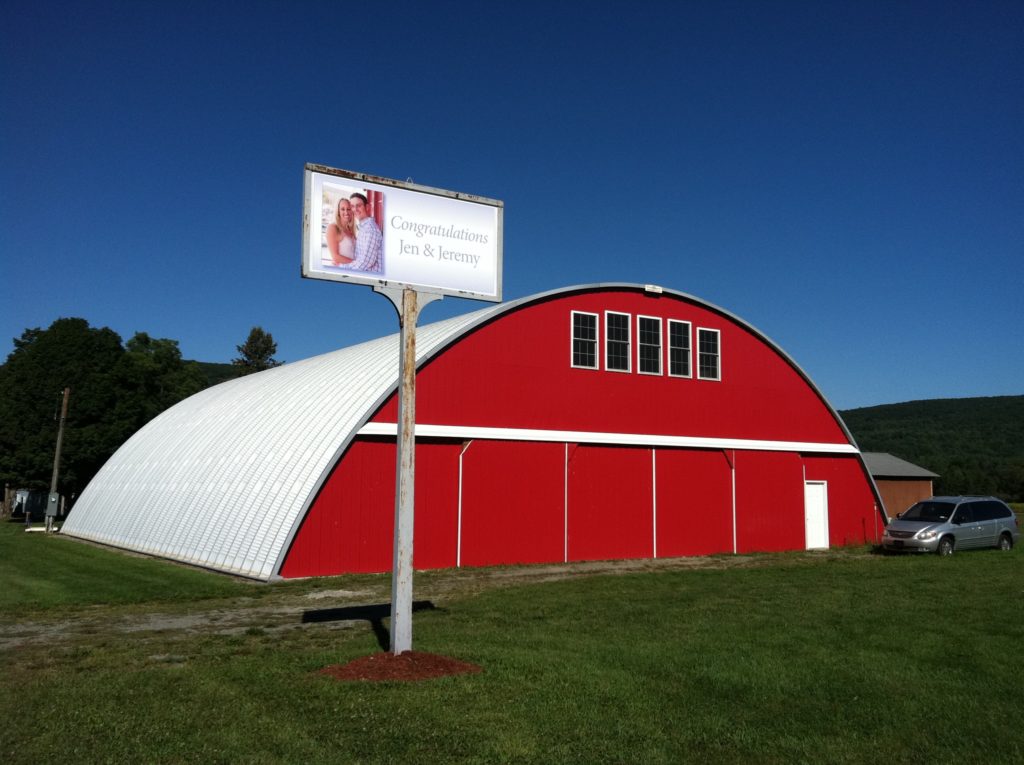 Q-model Quonset hangar with custom red endwall, upper windows, white entrance door.