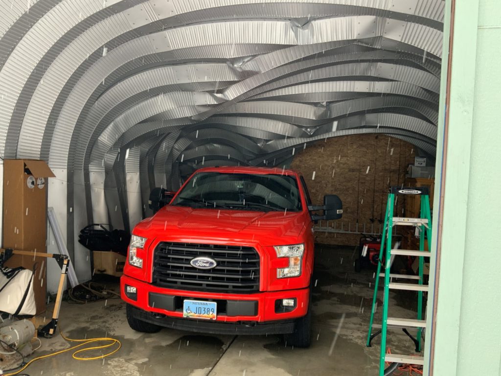 Inside a Quonset garage with bent ceiling arches sheltering red truck.