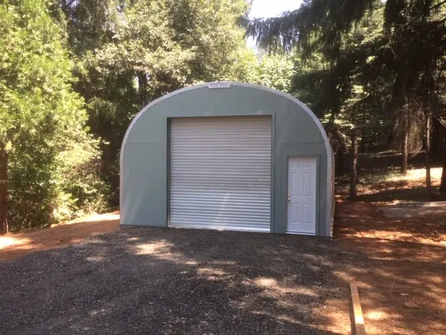 Custom sage green endwall Quonset garage with rolling door and white entrance door.