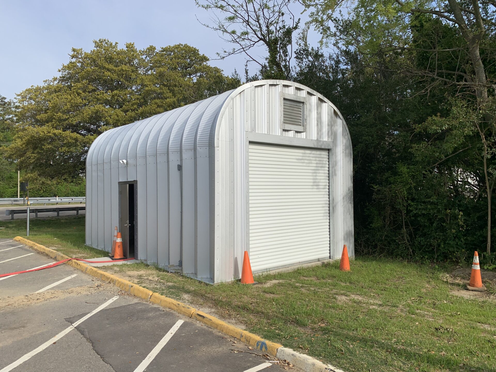 S-Model Quonset hut with man door on the side, five traffic cones, and a yellow-painted curb.