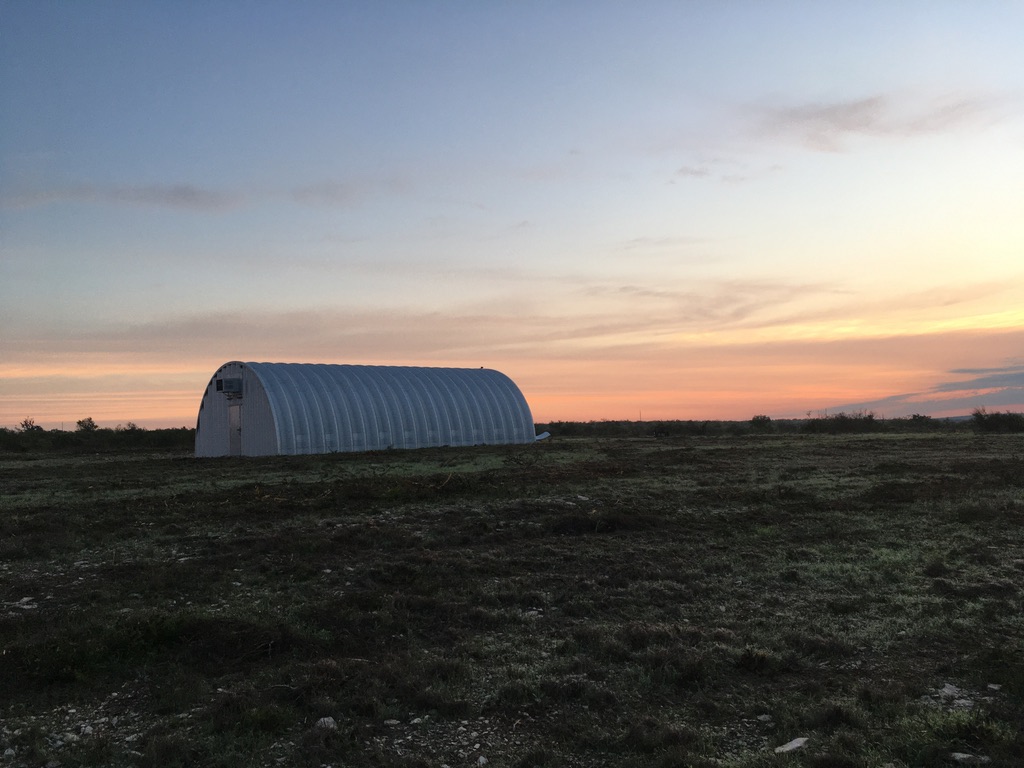 Side view of Q-Model Quonset hut with background of sunset.