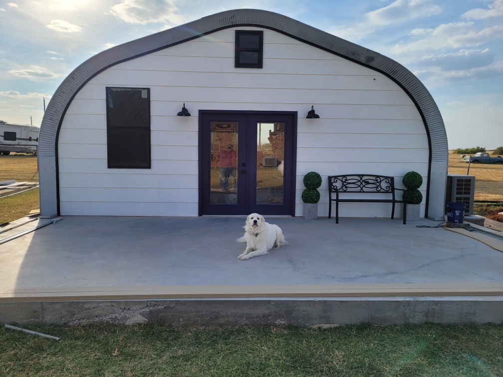 A-frame house with custom white recessed endwall and purple double doors and a white dog laying in front on a concrete slab