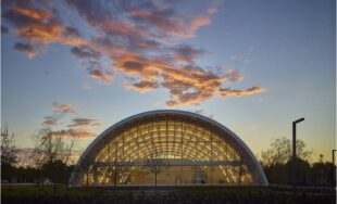 Front view of Q-Model Quonset hut with custom glass end wall and clouds in the background