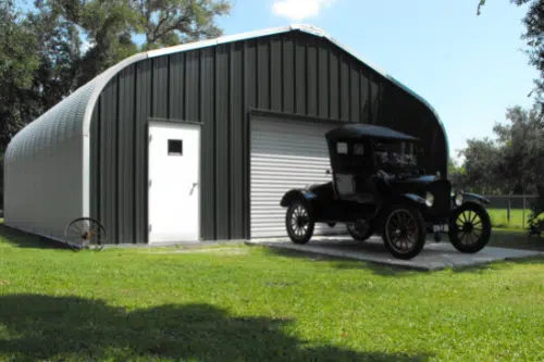 A-Model Quonset hut with custom gray endwall, white entry door and white garage door with vintage black vehicle in front of it.