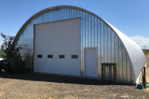 Q-model Quonset garage with metal endwall, tall garage door, and white entrance door.