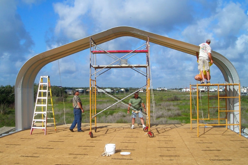 Three men building A-Model Quonset hut with scaffolding and a ladder