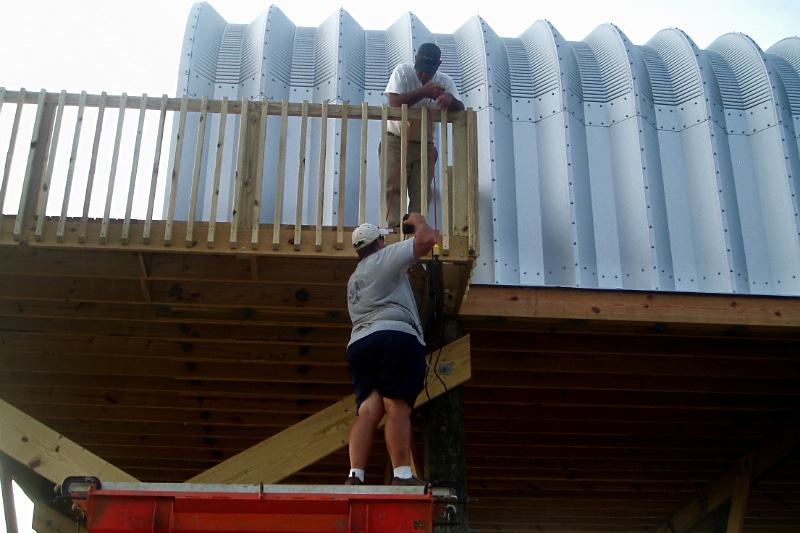 Two men constructing wooden balcony outside of their Quonset hut