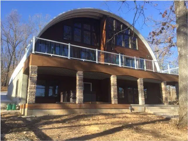 Two story S-model Quonset home with custom endwall, stone pillars, and a balcony.