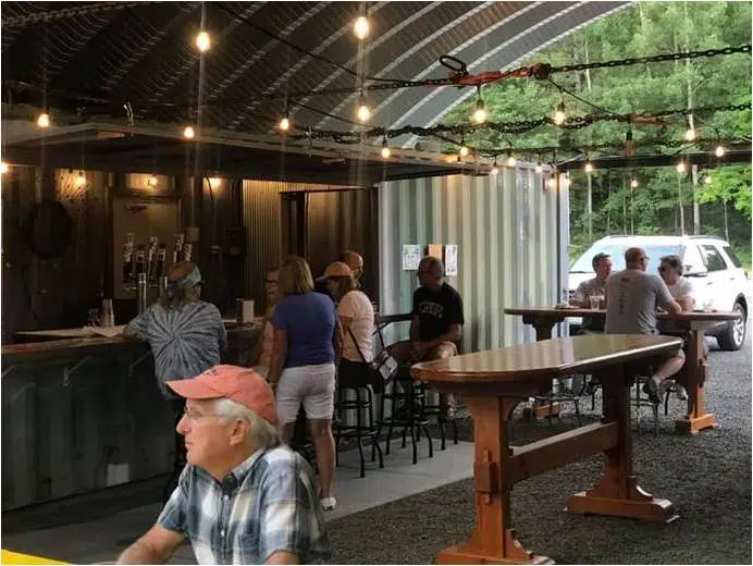 Inside of shipping container brewery: people gathered around tables and bar under suspended lights.