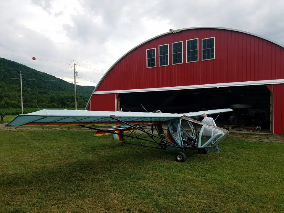 Custom red endwall with upper windows on Q-model Quonset hangar with large center opening, small plane in front.