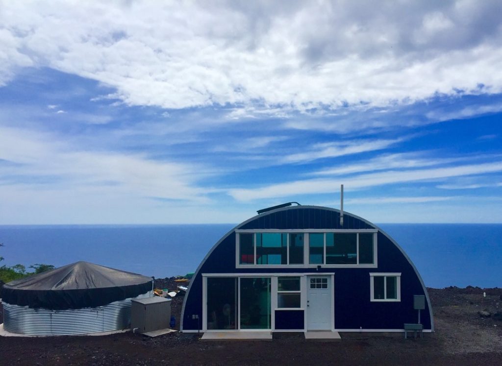 Q-model Quonset home near ocean, custom red endwall with windows, sliding glass door, and white entrance door.