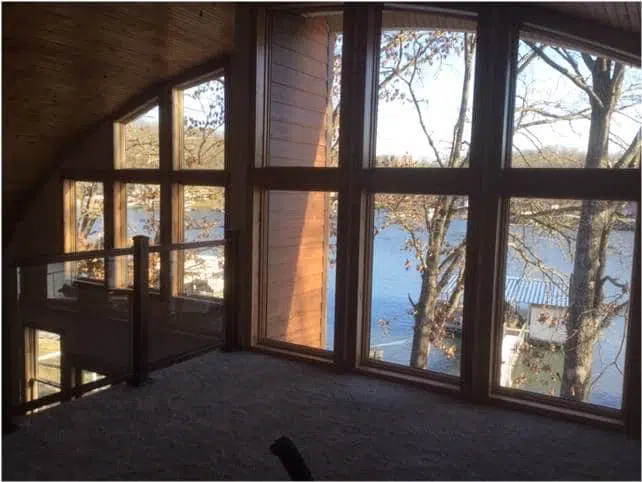 Inside a Quonset home: loft view overlooking lake through custom endwall windows.