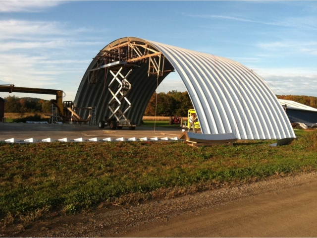 Assembling of large Quonset hangar, lift and wooden trusses holding arches in position.