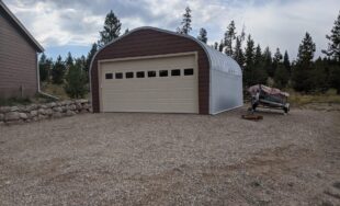 A-Model Quonset hut with brown end wall, tan garage door, and small boat next to the Quonset hut.