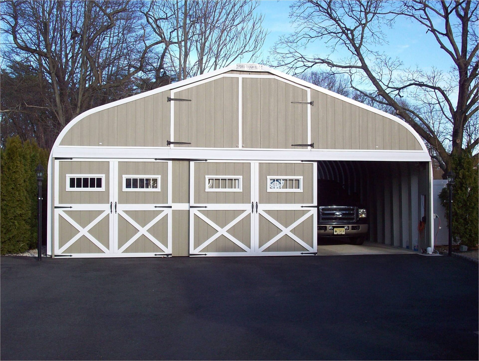 A-Model Quonset hut with two doors for a garage, doors bordered in white, and a black truck in the right garage door.
