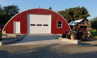 q model steel hay storage building with custom red front endwall and tractor outside