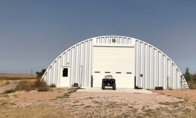 Q-Model workshop with a steel end wall, white entry door, and white garage door, with an ATV parked out front