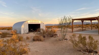 S-Model Quonset hut with open garage door, tumbleweeds on the ground, a canopy on the right, and shovels leaning against the building.