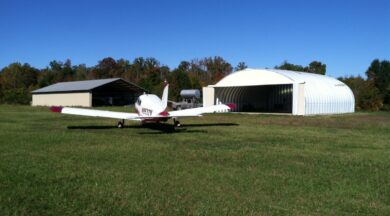 wide s-model quonset hut hangar with sliding doors that are open with a red and white airplane in the forefront