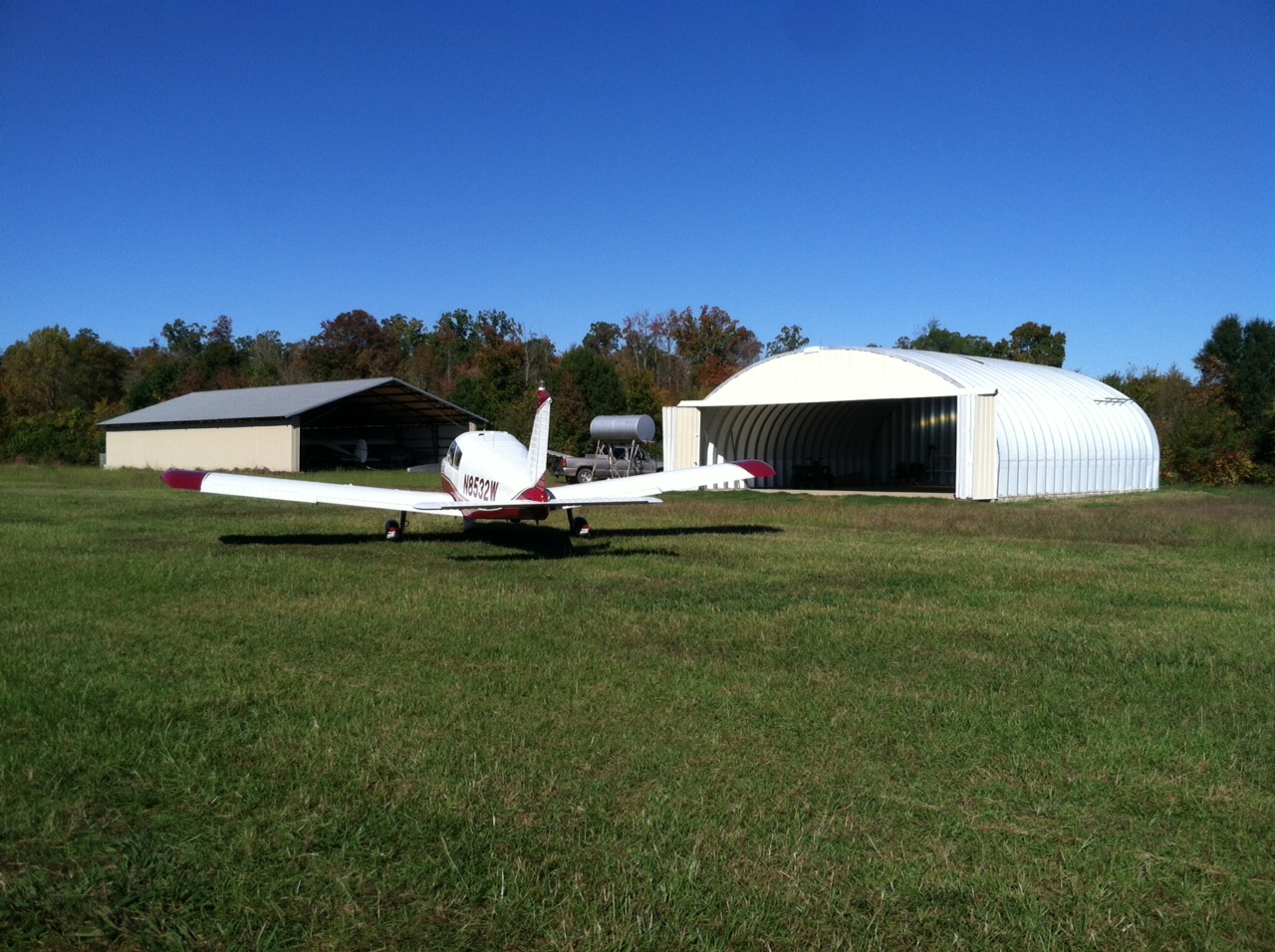 wide s-model quonset hut hangar with sliding doors that are open with a red and white airplane in the forefront